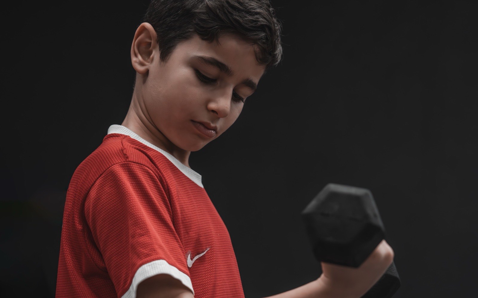 Kırmızı spor tişörtüyle dambıl kaldıran genç sporcu