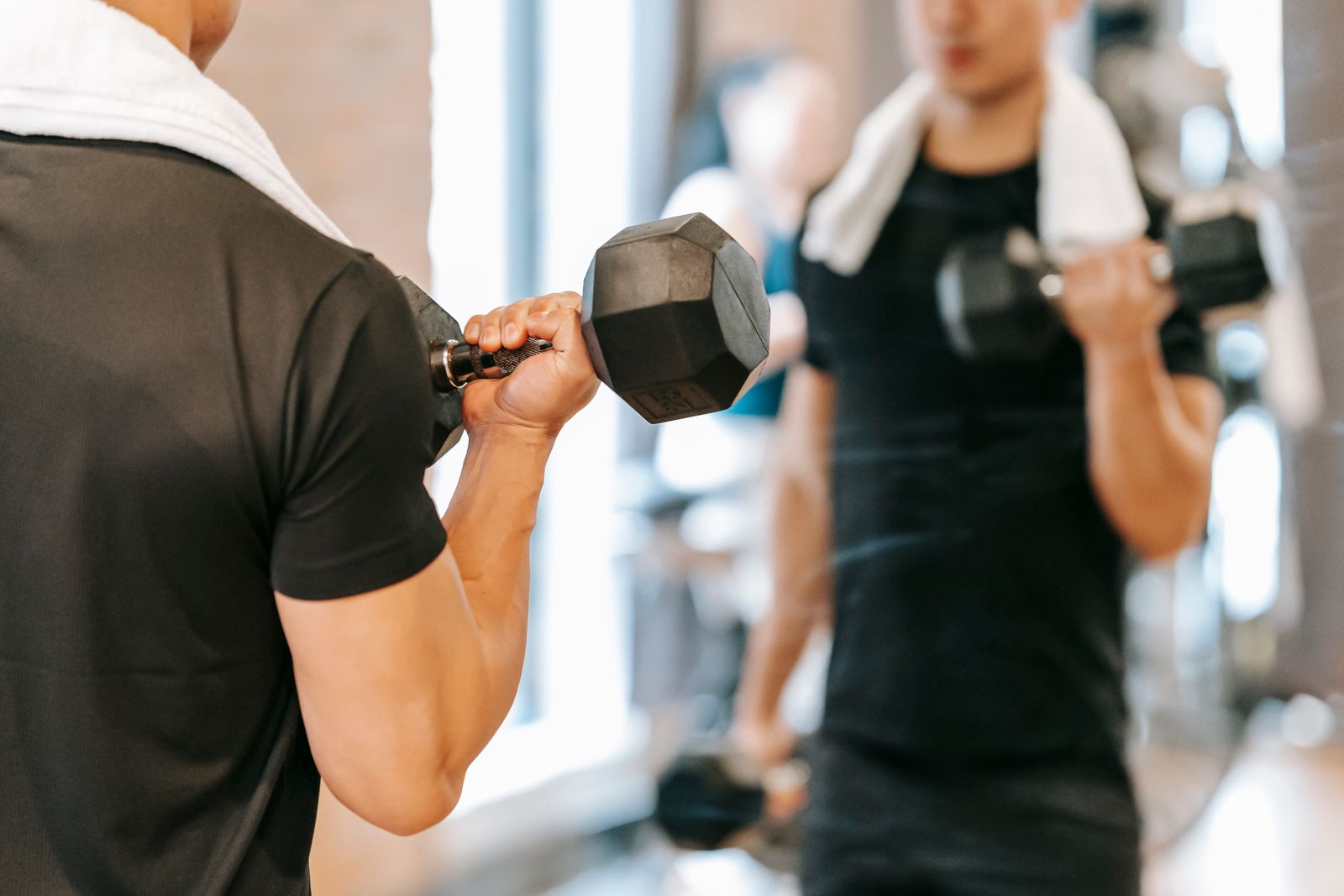 Spor salonunda ayna karşısında dambılla biceps curl yapan sporcu